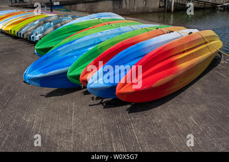 Una fila di vivacemente policroma kayak seduto a terra, inclusi i colori rosso, verde e blu Foto Stock