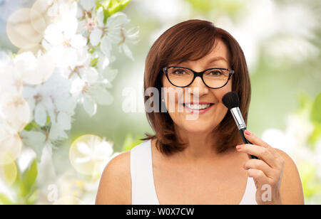 Sorridente donna senior con make up pennello fard Foto Stock