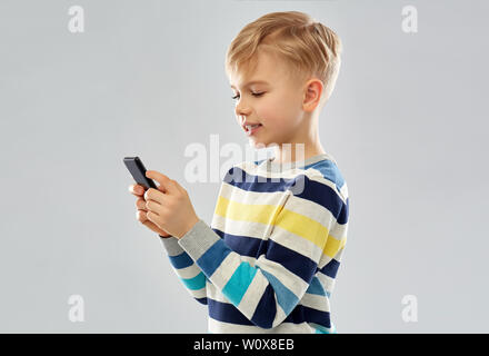 Little Boy in striped pullover utilizza lo smartphone Foto Stock