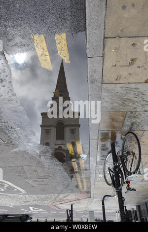 La riflessione della Chiesa di Cristo inn spitalfields pozzanghera con una bici su un marciapiede Foto Stock