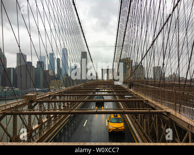 Guardando verso Manhattan sul ponte di Brooklyn come un giallo taxi passa al di sotto di Foto Stock