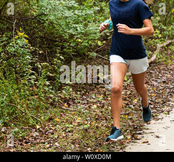 Una femmina di distanza runner è in esecuzione su una sporcizia e percorso di erba con foglie sul terreno. Foto Stock