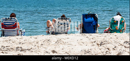 Vista da dietro di quattro donne rilassante in sedie da spiaggia che si affaccia sull'oceano presso la spiaggia. Foto Stock