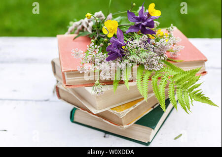 Estate composizione vintage. Libri antichi, un bouquet di fiori selvatici su un sfondo rustico. Foto Stock