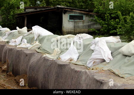 La linea di una protezione antiesondazione temporanea parete realizzata con scatola di barriere e sacchi di sabbia coperte di fitti panno in geotessile e nylon utilizzato per proteggere case famiglia Foto Stock