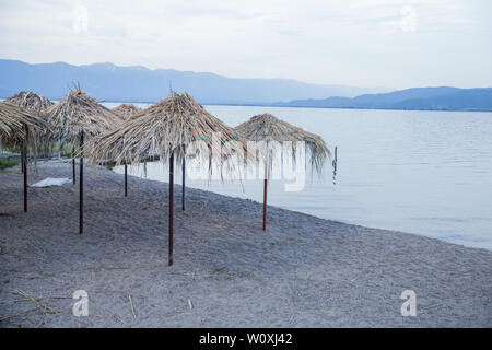 Spiaggia con ombrellone a Doiran Lake Shore nel nord della Macedonia in estate al tramonto. Foto Stock