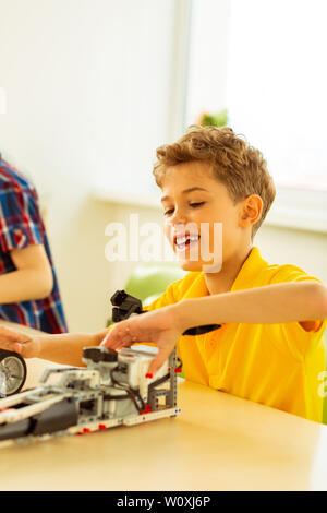 Così felice. Allegro ragazzo positiva avente un sacco di divertimento durante la costruzione del modello di auto Foto Stock