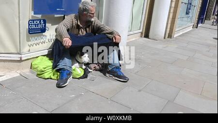 Un mendicante si trova al di fuori di un negozio a Buxton, Derbyshire Foto Stock