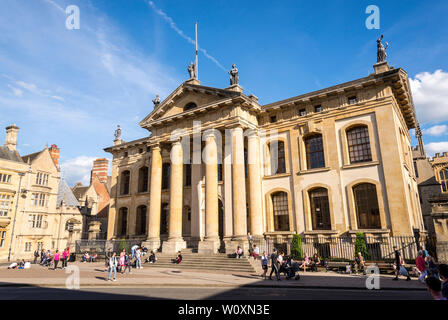 Persone sedersi sui gradini nella parte anteriore dell'edificio Clarendon vivacemente illuminate dal sole su di una splendida giornata estiva nella famosa città universitaria di Oxford Foto Stock