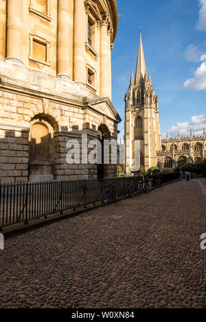 Una bella sera d'estate nella famosa città universitaria di Oxford. Il soleggiato luminosamente Radcliffe Camera e di Santa Maria la Chiesa con paralume in primo piano. Foto Stock