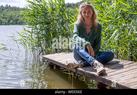 Mirow, Germania. Il 28 giugno, 2019. L'attrice Petra Schmidt-Schaller siede su un molo durante una pausa per riprese il quattro-parte la criminalità mini-serie 'Die Toten von Marnow'. L'NDR/ARD Degeto co-produzione è circa una serie di omicidi e uno scandalo di vecchia Stasi persone, servizi segreti e dell'industria farmaceutica. La produzione avrà luogo nel Meclemburgopomerania occidentale di Berlino e della Bassa Sassonia e si aspetta di essere mostrato su ARD in autunno 2020. Credito: Jens Büttner/dpa-Zentralbild/dpa/Alamy Live News Foto Stock