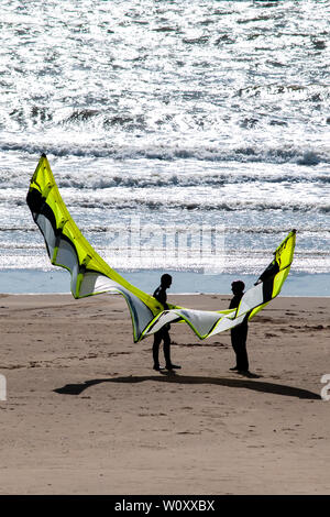 Kite surfers permanente sulla Aberavon Sands tenuta su un aquilone usato per praticare il kitesurf. Onde può essere visto la rottura sulla spiaggia sabbiosa. Swansea Bay. Foto Stock