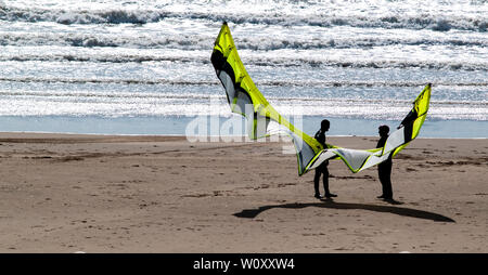 Kite surfers permanente sulla Aberavon Sands tenuta su un aquilone usato per praticare il kitesurf. Onde può essere visto la rottura sulla spiaggia sabbiosa. Swansea Bay. Foto Stock