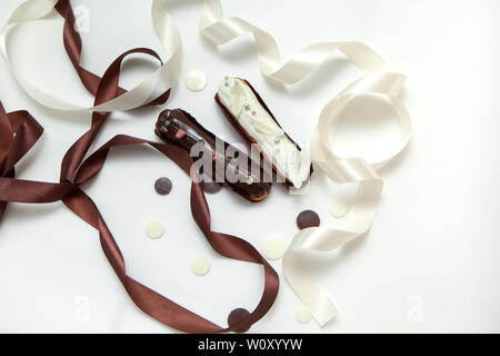 Close-up di un set di due eclairs con diversi ripieni e design isolare su una superficie bianca decorata con gocce di cioccolato, bianco e marrone di seta ri Foto Stock