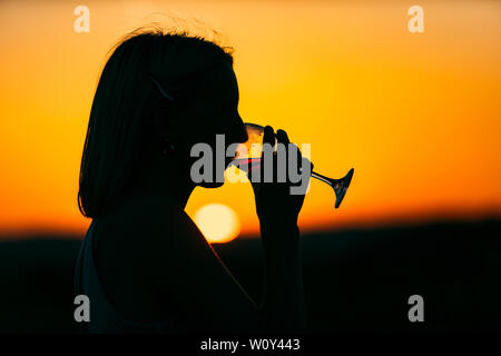 Silhouette di una giovane ragazza di bere da un bicchiere di vino Foto Stock