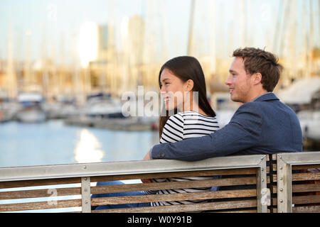 Coppia romantica seduta sul banco in porto vecchio, Port Vell di Barcellona, in Catalogna, Spagna. Felice l'uomo e la donna che abbraccia per godersi la vita e il romanticismo all'esterno. Multirazziale caucasico coppia asiatica nell'amore. Foto Stock