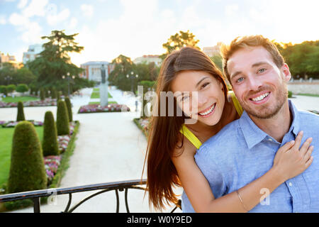 Ritratto di coppia romantica abbracciando in amore guardando la fotocamera. Multiculturale di uomo e donna sorridente felice di El Retiro a Madrid, Spagna, Europa. Ragazza asiatica, giovane uomo caucasico. Foto Stock