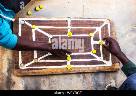 Tradizionale strategia africana board game sapere come morabaraba o muravarava essendo giocato su una tavola di legno con tappo di bottiglia pezzi Foto Stock