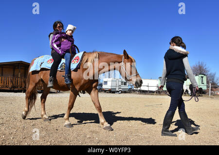 Equitazione La terapia per bambini portatori di handicap. Ragazza con paralisi cerebrale su un cavallo con il suo terapeuta, la giovane madre che conduce il cavallo Foto Stock