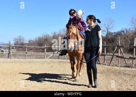 Equitazione La terapia per bambini portatori di handicap. Ragazza con paralisi cerebrale su un cavallo con il suo terapeuta, la giovane madre che conduce il cavallo Foto Stock