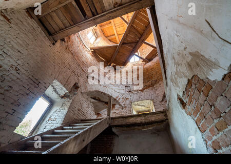 Ampie e spaziose abbandonato vuoto sala nel seminterrato del palazzo antico o palazzo con incrinato intonacate pareti in mattoni, piccole finestre, il pavimento era sporco e st in legno Foto Stock