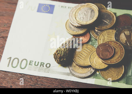 Una cannabis bud giace su un centinaio di euro bill e monete di close-up. Acquisto e vendita della legalizzazione delle droghe leggere. la cannabis medica La concezione di business. Foto Stock