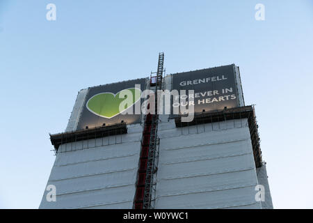 Grenfell Tower, ora coperta, con il simbolico cuore verde visualizzato. "Per sempre nei nostri cuori" Foto Stock