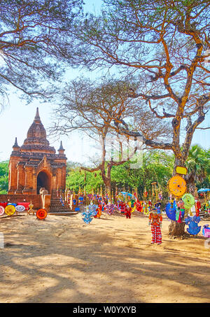 La grande quantità di autentici souvenir birmano - marionette a filo e ombrelli dipinti appesi sugli alberi nel sito archeologico di Bagan, Myanmar Foto Stock