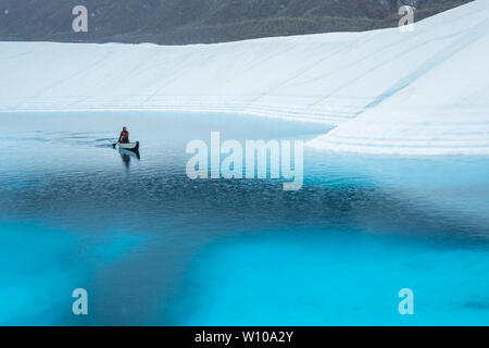 Pagaiando attraverso un lago supraglacial sul ghiacciaio Matanuska sotto la pioggia. Ice Climber corssing un profondo lago blu getting piovuto a. Foto Stock