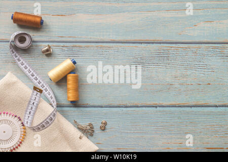 Accessori per il cucito e tessuti su uno sfondo blu. Tessuto, fili di cucitura, ago, perni, pulsanti e la cucitura di centimetro. top view, flatlay, copyspace Foto Stock