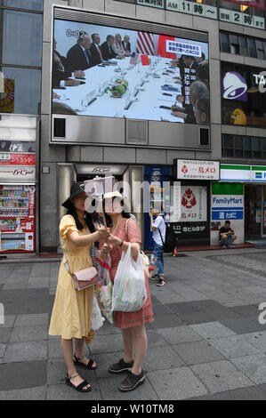 Osaka, Giappone. Il 29 giugno, 2019. Due turisti cinesi prendere un selfie mentre un aggiornamento di notizie del G20 riunione tra il presidente statunitense Donald Trump e il presidente cinese Xi Jinping è stata annunciata su un grande schermo a Namba di Osaka in Giappone. Lo stesso giorno i presidenti, primi ministri e altri alti dirigenti provenienti da tutto il mondo si sono riuniti per la seconda giornata della Osaka vertice G20. Foto scattata su Sabato, 29 giugno 2019. Foto di: Ramiro Agustin Vargas Tabares Credito: Ramiro Agustin Vargas Tabares/ZUMA filo/Alamy Live News Foto Stock