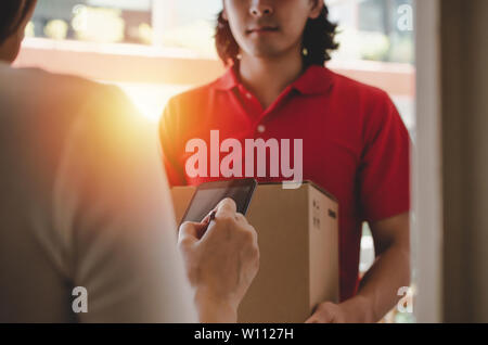 Giovane donna cliente apponendo la firma digitale nel telefono mobile che riceve il pacco postale box dal corriere con servizio di consegna a domicilio di uomo volto sorridente Foto Stock