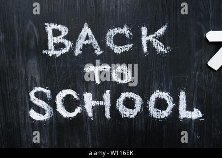 Si torna a scuola una frase scritta su di un legno nero sfondo, vista dall'alto. Il nuovo semestre, il concetto di istruzione: laici piana di parole scritte a mano e pezzi di Chalk Foto Stock