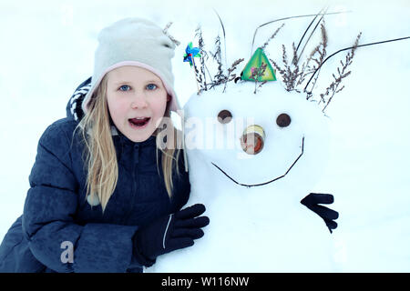 Ragazza fa un pupazzo di neve al di fuori in inverno. ragazza e pupazzo di neve sono sorridente Foto Stock