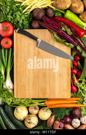 Coltello per cuoco sul tagliere di legno con verdure fresche dello sfondo. Mangiare sano concetto. Vegetariano cibo crudo. Foto Stock