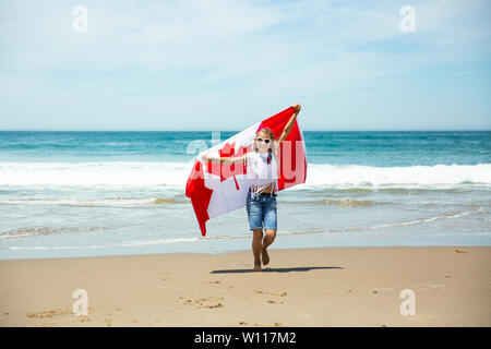 Felice ragazza canadese porta svolazzanti bianco rosso bandiera del Canada contro il cielo blu e Sfondo oceano. Bandiera canadese è un simbolo di libertà e la libertà Foto Stock