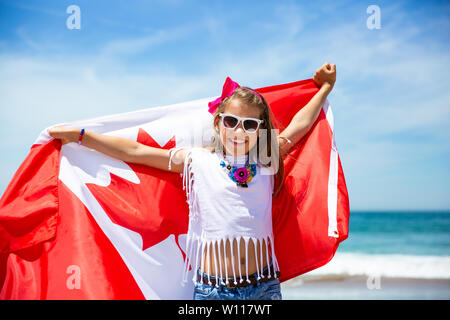 Felice ragazza canadese porta svolazzanti bianco rosso bandiera del Canada contro il cielo blu e Sfondo oceano. Bandiera canadese è un simbolo di libertà e la libertà Foto Stock