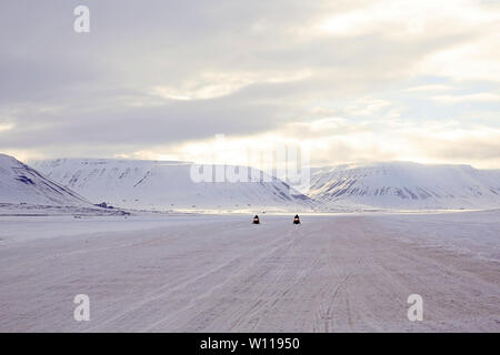 Due motoslitte si avvicina, montagne innevate sullo sfondo. Svalbard, Norvegia Foto Stock