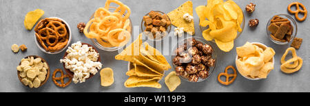 Assortimento di spuntini malsana: chips, popcorn, nachos, salatini, anelli di cipolla in ciotole, vista dall'alto, banner. Mangiare malsano concetto. Foto Stock