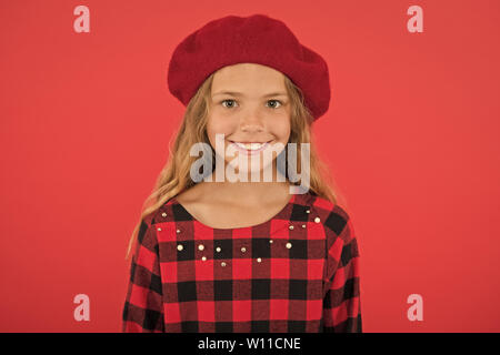 Kid poco carino ragazza sorridente in posa di hat sfondo rosso. Moda beret accessorio per la femmina. Come indossare il francese beret. Beret style ispirazione. Come indossare beret come moda ragazza. Foto Stock