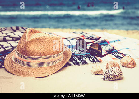 Cappello di paglia, occhiali da sole e copertura beachwear avvolgere su una spiaggia tropicale con conchiglie di mare Foto Stock