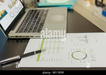 Documenti aziendali grafici finanziari, analisi statistica sulla scrivania con computer laptop con grafici, diagrammi e grafici sullo schermo. Foto Stock