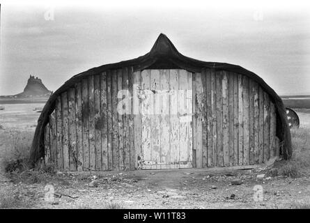 Holy Island Northumberland 1970S.. Un tradizionale capannone per barche dei pescatori realizzato con una vecchia barca per aringhe capovolta, il castello di Lindisfarne all'orizzonte, 1971. Regno Unito. HOMER SYKES Foto Stock