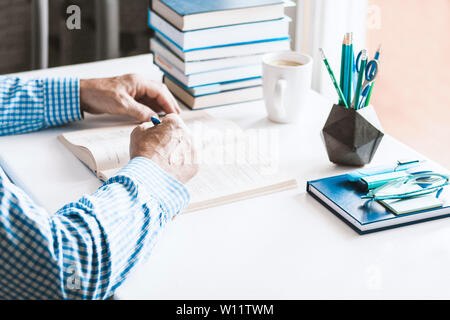 Uomo in camicia blu la lettura di un libro sul moderno ed elegante luogo di lavoro con forniture da ufficio e di libri, scrivania concetto di lavoro nei colori bianco e blu Foto Stock