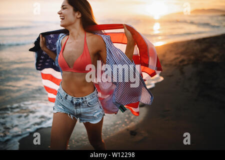 Allegra donna felice all'aperto sulla spiaggia tenendo bandiera degli Stati Uniti avendo divertimento. Foto Stock