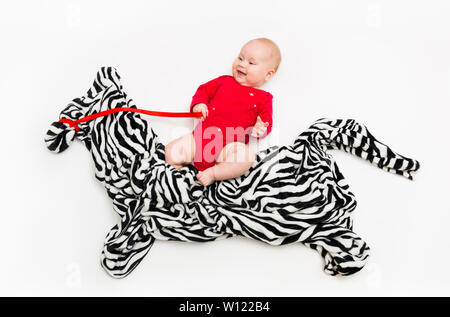 Un quattro-mese-vecchio bambino cavalca una Zebra da un panno sul pavimento Foto Stock