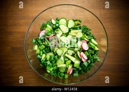 Insalata fresca di cetrioli e verdi in una piastra su un tavolo di legno Foto Stock