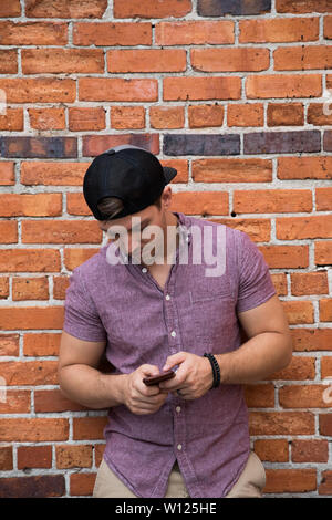 Bel giovane uomo caucasico con Indietro Hat sorridere per ritratti di fronte a trama un muro di mattoni al di fuori Foto Stock