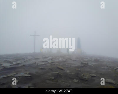 Grande Croce e la sagoma di un uomo come visto attraverso la nebbia sulla sommità del picco Hoverla, 2061m, Carpazi, Ucraina. Foto Stock