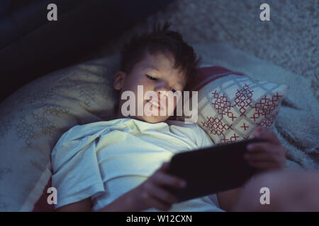 Little Boy giocando sulla tavoletta digitale di notte in camera da letto Foto Stock